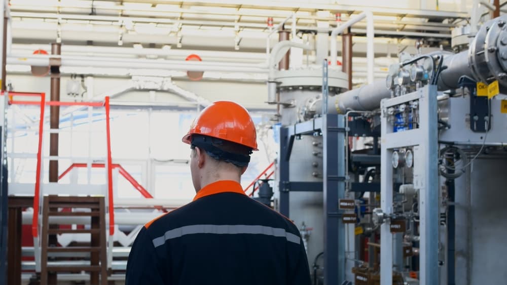 Worker in orange helmet and overalls inspecting equipment in a chemical plant