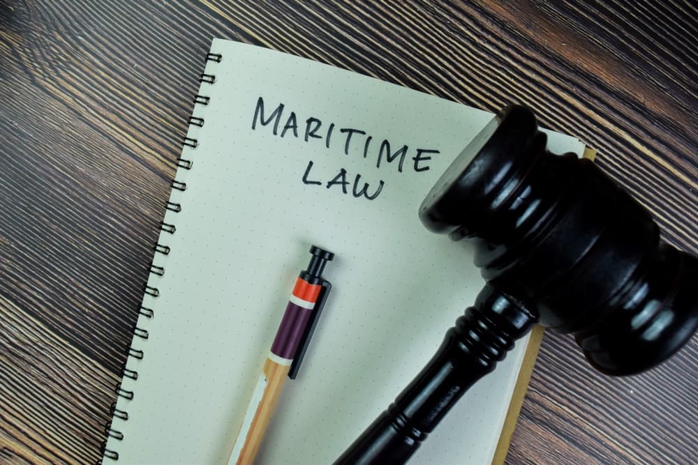 The concept of maritime law is inscribed on a book beside a gavel, both isolated on a wooden table.






